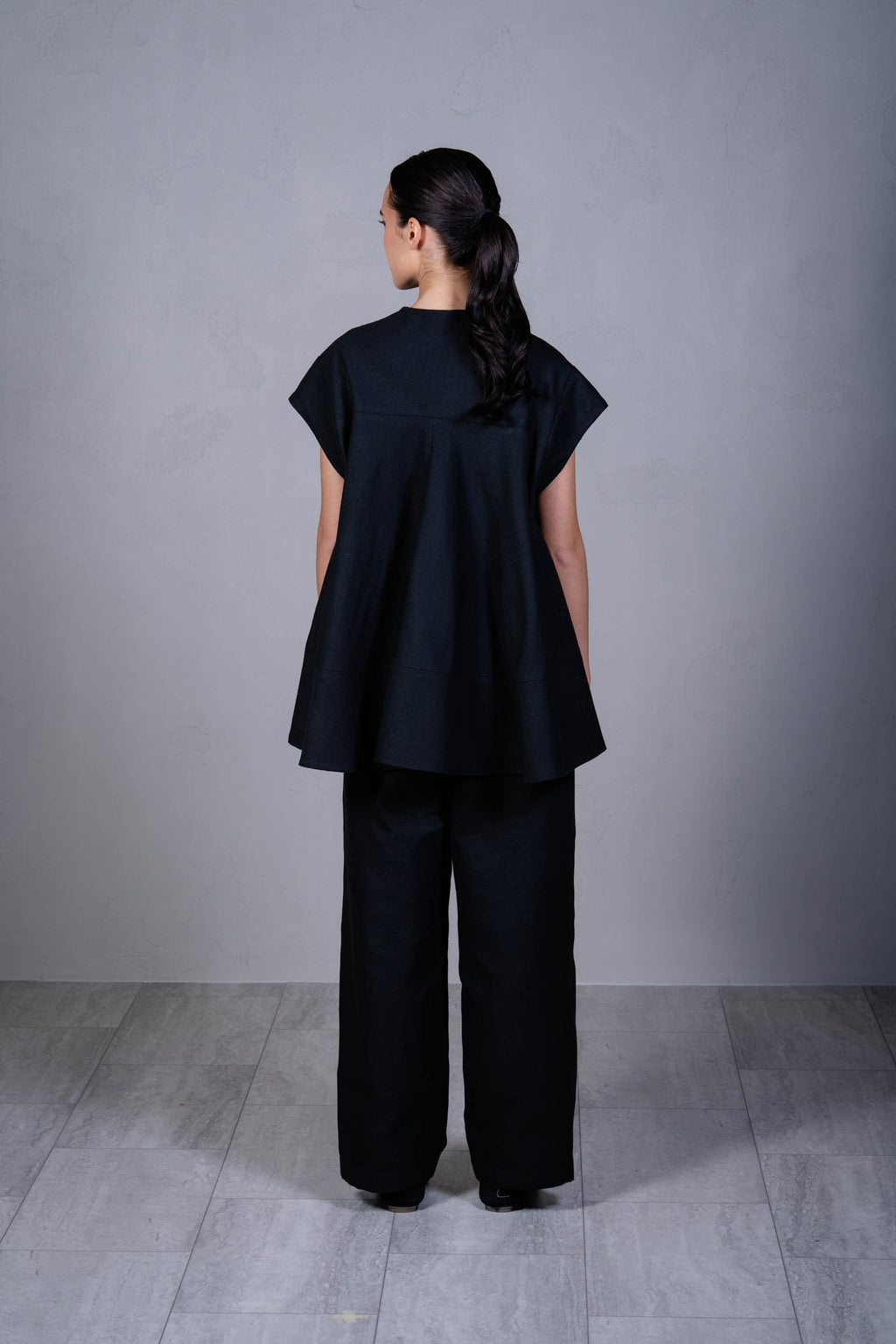 Person wearing a black outfit standing against a gray background