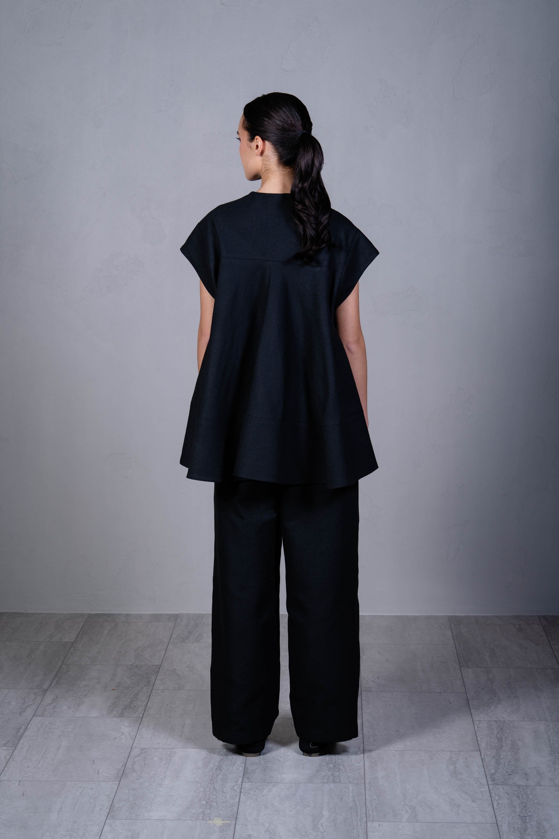 Person wearing a black outfit standing against a gray background