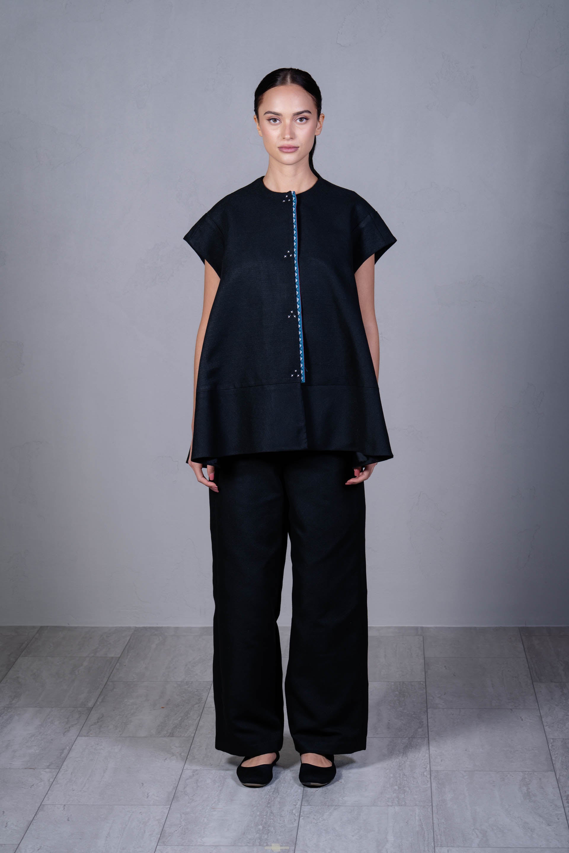 Model wearing a black outfit with a textured top and wide-leg pants on a gray background